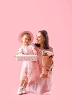 Şirin küçük kızı, güzel annesini hediye kutusu ve pembe arka planda bir buket gülle selamlıyor. Anneler Günün kutlu olsun.