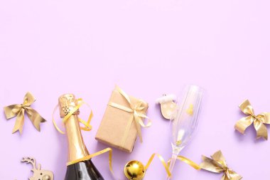 Cam kaplı bir şişe şampanya, Noel süslemeleri ve leylak arkaplanlı bir hediye kutusu.