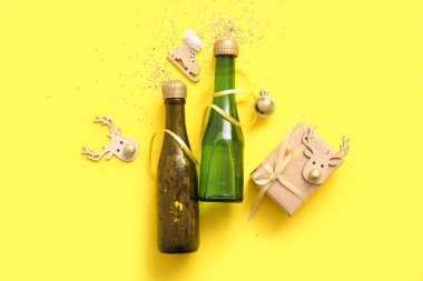 Noel süslemeleri ve sarı arka planda hediye kutusu olan şampanya şişeleri.