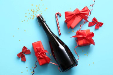 Bir şişe şampanya, baston şekerler, fiyonklar ve mavi arka planda Noel hediyesi kutuları.