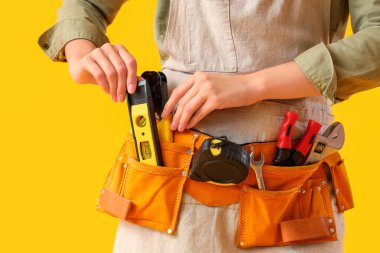 Sarı arkaplanda alet çantası olan kadın işçi, yakın plan.