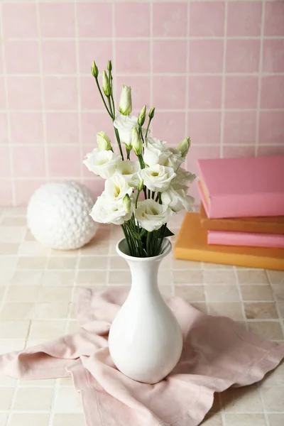 Vase with beautiful eustoma flowers, books and decor on color tile background