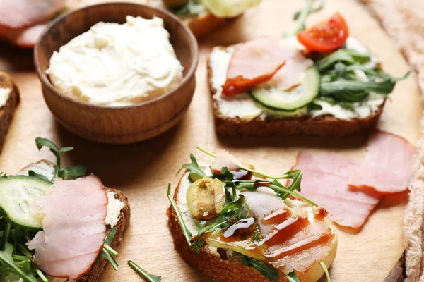 Wooden board with delicious sandwiches and cream cheese, closeup