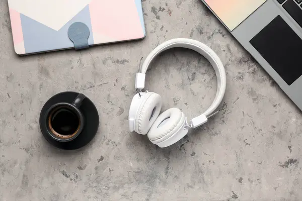Modern white headphones with laptop and notebook on grey grunge background