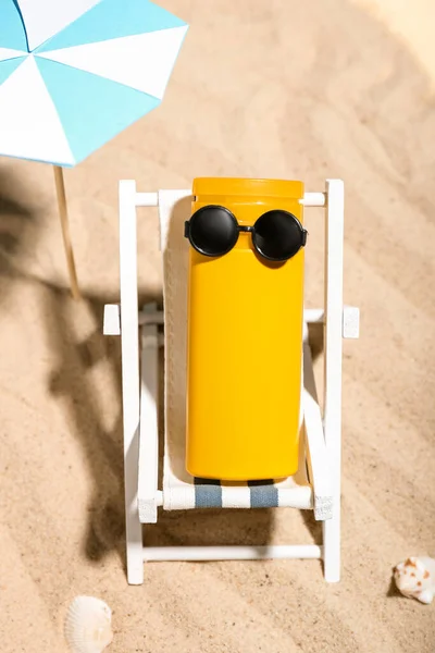 Creative composition with miniature deckchair, umbrella and sunscreen on sand
