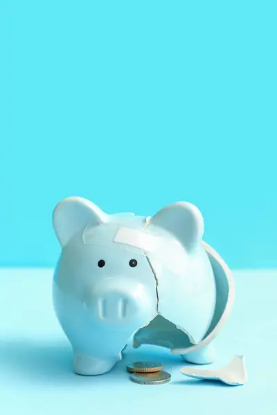 Broken patched piggy bank with money on blue background. Bankruptcy concept
