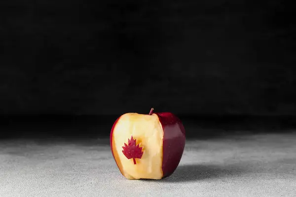Apple with cut maple leaf on black and white background. Canadian flag concept