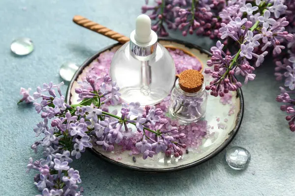 Bottles of cosmetic oil with beautiful lilac flowers and sea salt on blue table