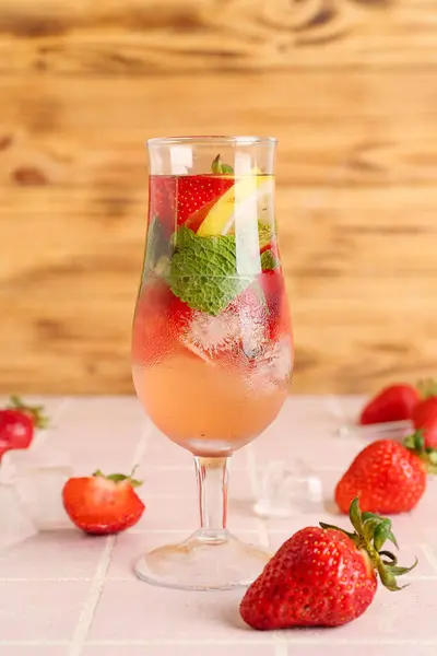 Glass of fresh lemonade with strawberry and lemon on pink tile table