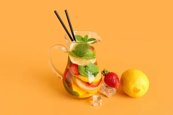 Jug of fresh lemonade with strawberry and lemon on orange background