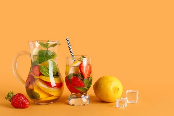 Glass and jug of fresh lemonade with strawberry on orange background