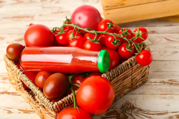 Wicker box with fresh tomatoes and bottle of juice on light wooden background