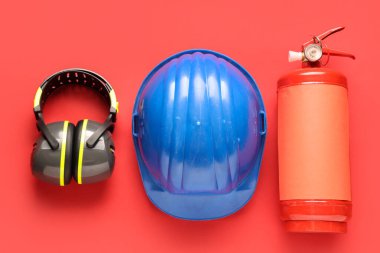 Yangın söndürücü, işitme koruyucular ve kırmızı arka planda miğfer.