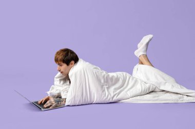 Eflatun arkaplanda dizüstü bilgisayar kullanan yakışıklı bir genç.