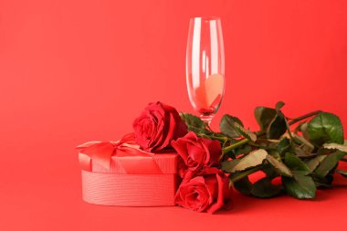 Bir buket güzel gül çiçeği, şampanya bardağı ve kırmızı arka planda kalp şeklinde hediye kutusu. Sevgililer Günü kutlaması