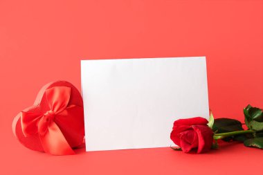 Boş tebrik kartı, güzel bir gül çiçeği ve kırmızı arka planda kalp şeklinde bir hediye kutusu. Sevgililer Günü kutlaması