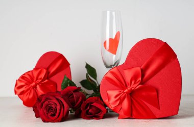 Bir buket güzel gül çiçeği, şampanya bardağı ve gri arka planda kalp şeklinde hediye kutusu. Sevgililer Günü kutlaması