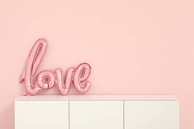 White cabinet with balloons in shape of word LOVE near pink wall. Valentine's Day celebration