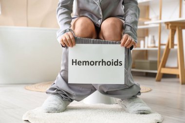Tuvaletteki klozette HEMORRHOIDS yazan kağıt tutan olgun bir kadın.