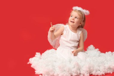 Aşk tanrısı gibi giyinmiş, kırmızı arka plandaki bir şeyi işaret eden sevimli küçük bir kız. Sevgililer Günü kutlaması