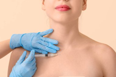 Bej arka planda boyundan enjeksiyon yaptıran genç bir kadın.