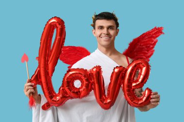 Aşk tanrısı gibi giyinmiş genç bir adam ve aşk kelimesi mavi arka planda balonlardan yapılmış. Sevgililer Günü kutlaması