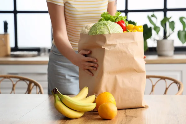 Young woman with paper bag of healthy food in kitchen, closeup