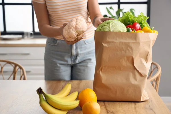 Young woman with paper bag of healthy food at table in kitchen, closeup