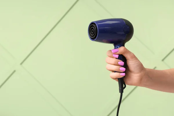 Female hand with hair dryer on green background