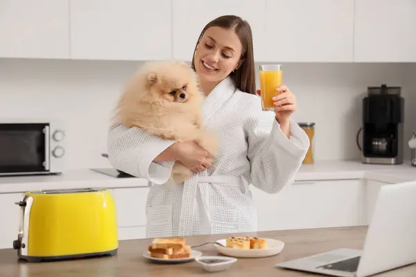 Young woman with cute Pomeranian dog having breakfast in kitchen