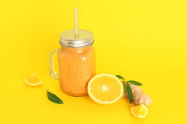 Sarı arka planda saman bulunan sağlıklı portakal suyu kavanozu.