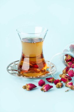 Açık mavi arkaplanda bir bardak Türk çayı ve kuru güller