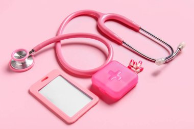 Stetoskop, ilaç organizatörü ve pembe arka planda rozet.