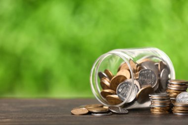 Masadaki bozuk paralarla bulanık yeşil doğa arka planına karşı devrilmiş. Tasarruf kavramı