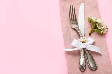 Çiçek açan ağaç dalı ve çatal bıçak takımı pembe arka planda peçeteyle katlanmış.