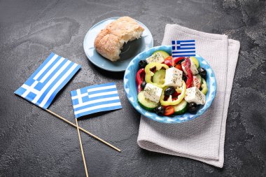 Bir kase peynirli salata, zeytin ve siyah grunge masasında Yunan bayrakları.