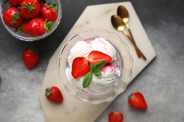 Bir kase vanilyalı dondurma, çilek, nane ve altın kaşıklar gri grunge masasında