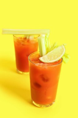Sarı arka planda kereviz ve limonlu Bloody Mary bardakları.