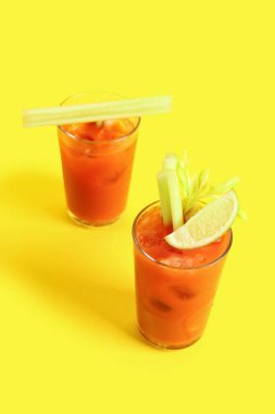 Sarı arka planda kereviz ve limonlu Bloody Mary bardakları.