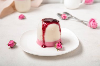 Böğürtlen soslu panna cotta tabağı ve beyaz masada güzel pembe gül çiçekleri.