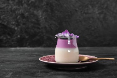 Bir bardak yaban mersinli panna cotta ve siyah masada güzel ortanca çiçekleri.