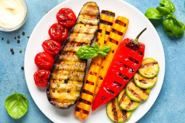 Izgara sebzeli tabak ve mavi arka planda fesleğen.