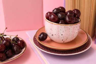 Pembe arka planda kitapları olan bir fincan ve bir tabak tatlı kiraz.