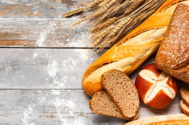 Gri ahşap masada farklı ekmek ve buğday kulakları.