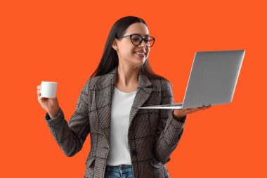 Dizüstü bilgisayarı ve turuncu arka planda bir fincan kahvesi olan güzel bir bayan programcı.