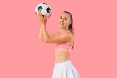 Pembe arka planda futbol topu olan mutlu, güzel, genç bir kadın.