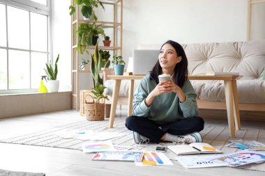 Elinde kahve fincanı olan genç Asyalı kadın evde çalışıyor.