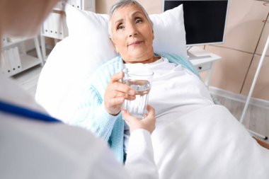 Yaşlı kadın huzurevindeki doktordan bir bardak su alıyor.