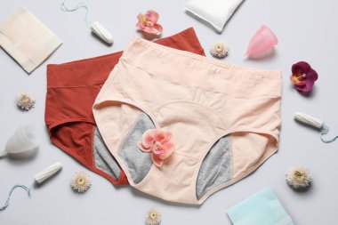 Dönem külotlu, pedli, tamponlu, regl bardaklı ve gri arkaplanlı güzel çiçekli kompozisyon