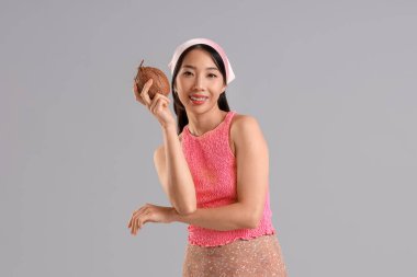 Gri arka planda hindistancevizi olan güzel bir Asyalı kadın.